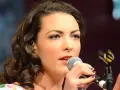 Caro Emerald śpiewa do mikrofonu, zbliżenie na twarz i dłonie.