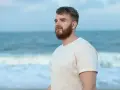 Mężczyzna z brodą na plaży, patrzący w dal. Arkadiusz - imię oznaczające "wielki władca", "wielki pan".