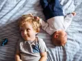 Dwóch braci, Emil i maluszek, leży na pasiastym kocyku. Emil ma blond włosy i uśmiecha się.