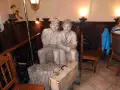 Dwie rzeźby siedzących mężczyzn, przypominających tońcio lub szczepcio, z akordeonem i walizką u stóp.