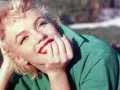 Marilyn Monroe, ikona kina, w zielonej sukience, z dłonią przy ustach, uśmiecha się promiennie.