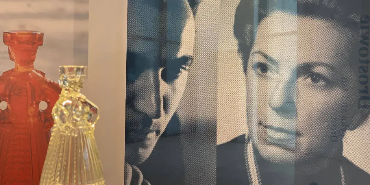 Szklana figura w kształcie sukni obok czerwonej postaci. W tle portret Eryki Trzewik Drost.