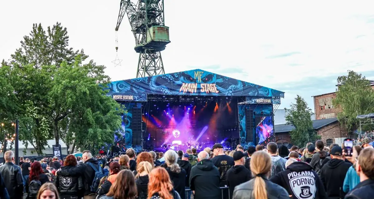 Tłum ludzi na koncercie pod wielkim dźwigiem. To jeden z wielu festiwali w Polsce, gdzie muzyka rockowa i metalowa przyciąga fanów.
