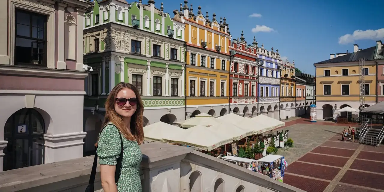 Kobieta na tle kolorowych kamienic Rynku Wielkiego w Zamościu. To miasto idealne, gdzie historia spotyka się z pięknem.