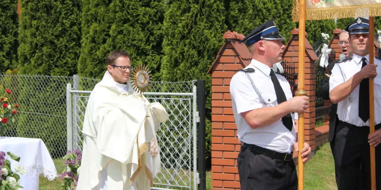 Ksiądz niesie monstrancję, a obok niego stoją policjanci. Może to być procesja, gdzie Krzysztof, jak jego imię znaczy "niosący Chrystusa", jest symbolem wiary.
