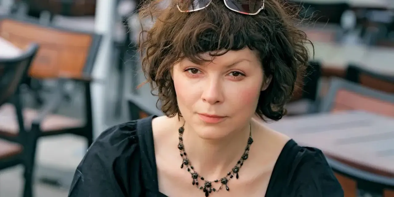 Agnieszka Glińska w czarnej sukience i naszyjniku, z okularami na głowie. Może wspominać swoich rodziców.