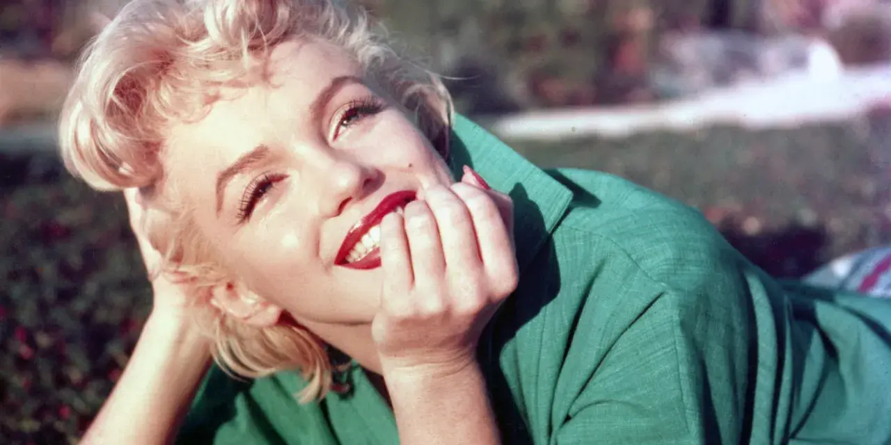 Marilyn Monroe, ikona kina, w zielonej sukience, z dłonią przy ustach, uśmiecha się promiennie.