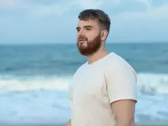 Mężczyzna z brodą na plaży, patrzący w dal. Arkadiusz - imię oznaczające "wielki władca", "wielki pan".