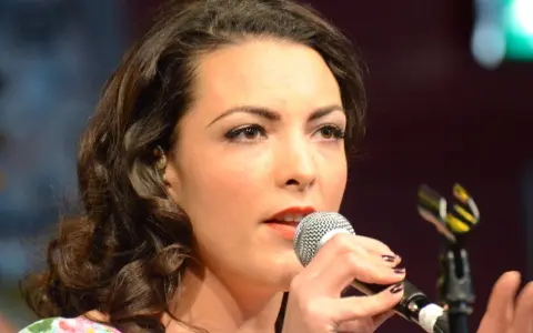 Caro Emerald śpiewa do mikrofonu, zbliżenie na twarz i dłonie.