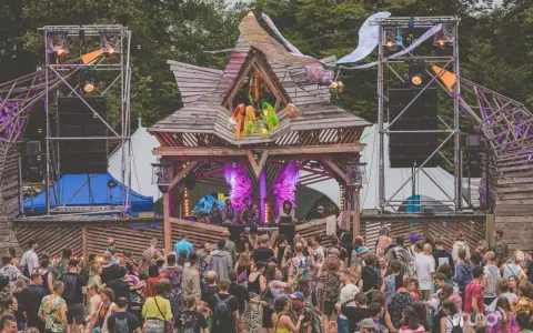 Tłum ludzi na festiwalu **summer contrast festival**. Drewniana scena z dekoracjami, głośniki i światła tworzą magiczną atmosferę.