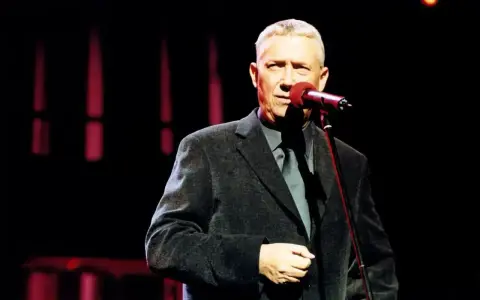 Mężczyzna w eleganckim garniturze śpiewa do mikrofonu. Może to być koncert z piosenkami Młynarskiego alfabetycznie.