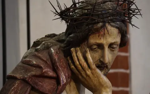 Chrystus Frasobliwy, rzeźba z koroną cierniową i krwawymi ranami, zamyślony, opiera głowę na dłoni.