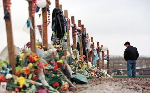 Pamięć o ofiarach masakry w Columbine High School. Krzyże ozdobione kwiatami i pamiątkami, obok stoi pogrążony w zadumie mężczyzna.