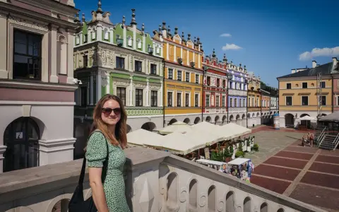 Kobieta na tle kolorowych kamienic Rynku Wielkiego w Zamościu. To miasto idealne, gdzie historia spotyka się z pięknem.