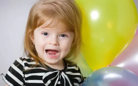 Uśmiechnięta dziewczynka, Natalia, z niebieskimi oczami i rudymi włosami, trzyma balony. Znaczenie imienia Natalia to "narodziny".