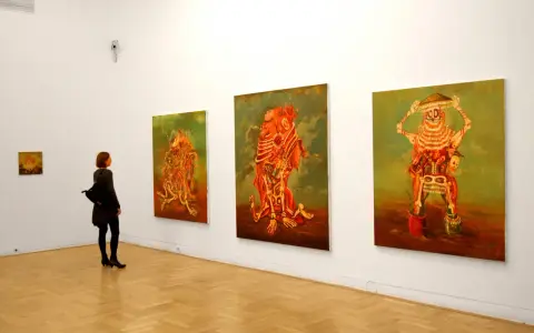 Kobieta podziwia surrealistyczne obrazy Jakuba Juliana Ziółkowskiego w galerii.