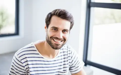 Uśmiechnięty mężczyzna o imieniu Marcin, z brodą i w pasiastym t-shircie, emanuje pozytywną energią. Znaczenie imienia Marcin to wojownik.