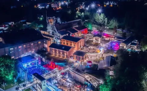 Nocny festiwal Carbon Silesia rozświetla postindustrialny krajobraz. Tłumy bawią się przy scenie, a kolorowe światła odbijają się od budynków dawnej kopalni.