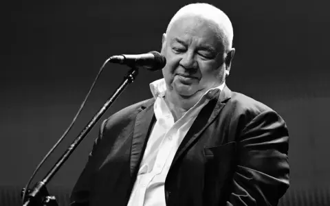 Czarno-białe zdjęcie Stanisława Sojki przy mikrofonie. Artysta z zamkniętymi oczami, w białej koszuli i marynarce, śpiewa. Stanisław Sojka nie żyje.