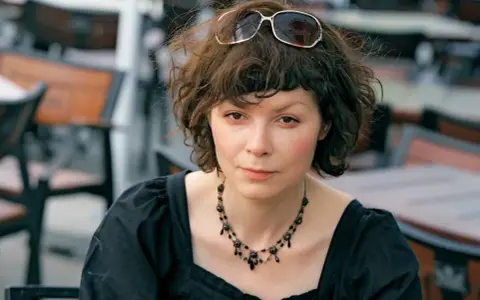 Agnieszka Glińska w czarnej sukience i naszyjniku, z okularami na głowie. Może wspominać swoich rodziców.