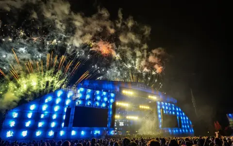Nocny koncert z fajerwerkami nad sceną. Tłum ludzi podziwia widowisko, a nad nimi rozbłyskują kolorowe petardy.