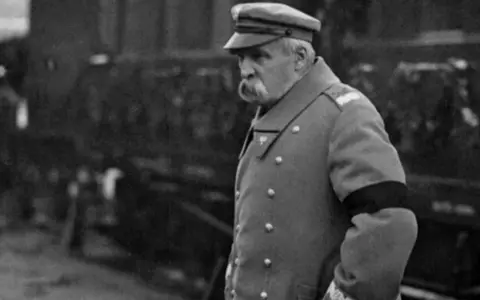 Marszałek Józef Piłsudski w mundurze, z czarną opaską na ramieniu, symbolizującą żałobę. W tle widać tłum ludzi, być może podczas uroczystości pogrzebowych, gdy Józef Piłsudski jak zmarł.