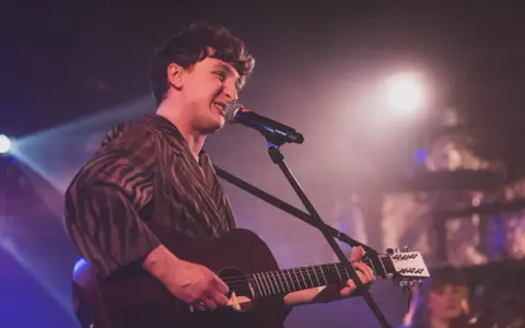 Wojtek Szumański na koncertach, śpiewający i grający na gitarze akustycznej.