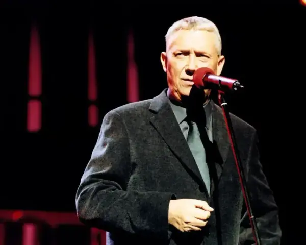 Mężczyzna w eleganckim garniturze śpiewa do mikrofonu. Może to być koncert z piosenkami Młynarskiego alfabetycznie.