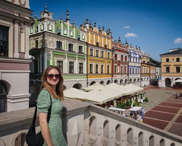 Kobieta na tle kolorowych kamienic Rynku Wielkiego w Zamościu. To miasto idealne, gdzie historia spotyka się z pięknem.
