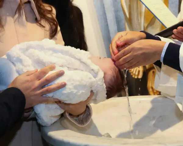 Chrzest dziecka, które może otrzymać imię Janina, symbolizujące łaskę Bożą. Woda spływa po jego głowie.