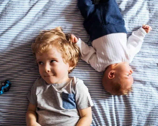 Dwóch braci, Emil i maluszek, leży na pasiastym kocyku. Emil ma blond włosy i uśmiecha się.