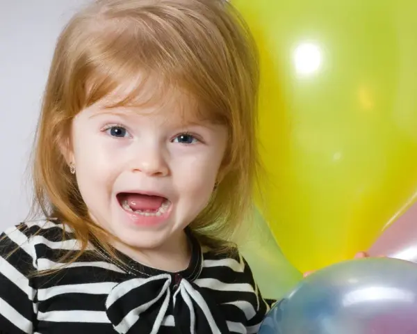 Uśmiechnięta dziewczynka, Natalia, z niebieskimi oczami i rudymi włosami, trzyma balony. Znaczenie imienia Natalia to "narodziny".