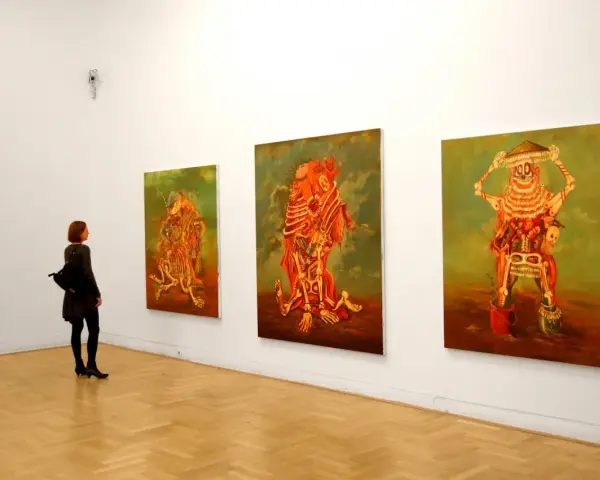 Kobieta podziwia surrealistyczne obrazy Jakuba Juliana Ziółkowskiego w galerii.