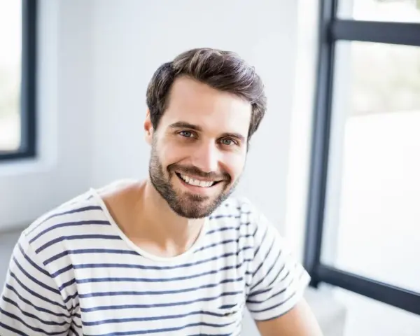 Uśmiechnięty mężczyzna o imieniu Marcin, z brodą i w pasiastym t-shircie, emanuje pozytywną energią. Znaczenie imienia Marcin to wojownik.