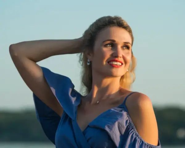 Uśmiechnięta Anita w niebieskiej sukience, z ręką we włosach. Jej imię, Anita, znaczy "łaska".