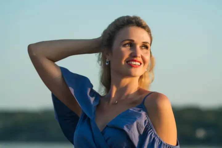 Uśmiechnięta Anita w niebieskiej sukience, z ręką we włosach. Jej imię, Anita, znaczy "łaska".