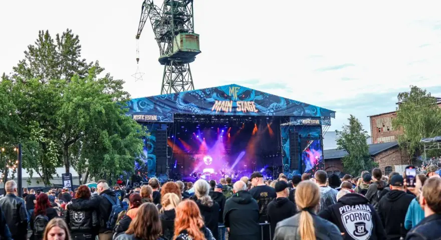 Tłum ludzi na koncercie pod wielkim dźwigiem. To jeden z wielu festiwali w Polsce, gdzie muzyka rockowa i metalowa przyciąga fanów.