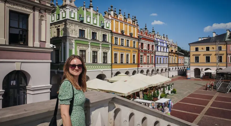 Kobieta na tle kolorowych kamienic Rynku Wielkiego w Zamościu. To miasto idealne, gdzie historia spotyka się z pięknem.