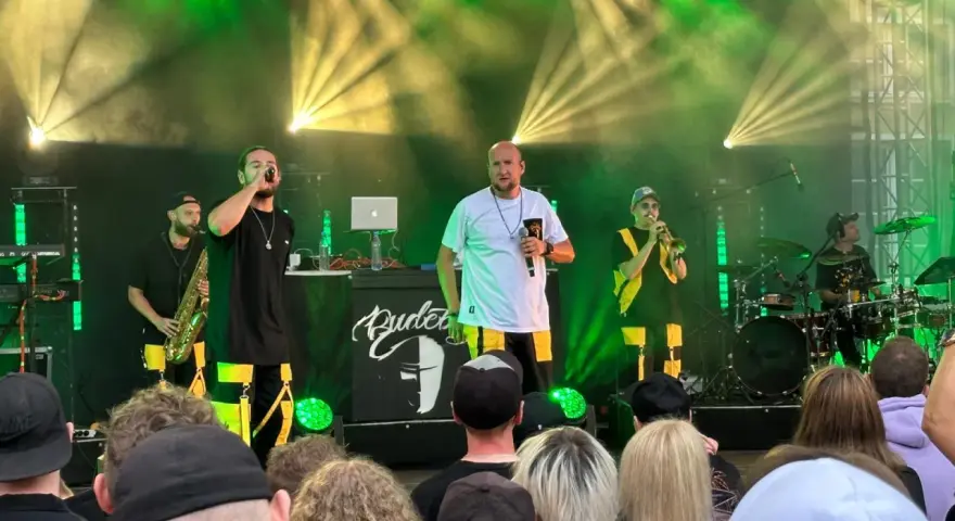 Zespół na scenie podczas festiwalu czochraj bobra fest. Wokalista śpiewa, grają saksofonista, trębacz i perkusista.