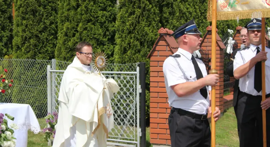 Ksiądz niesie monstrancję, a obok niego stoją policjanci. Może to być procesja, gdzie Krzysztof, jak jego imię znaczy "niosący Chrystusa", jest symbolem wiary.