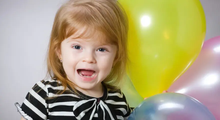 Uśmiechnięta dziewczynka, Natalia, z niebieskimi oczami i rudymi włosami, trzyma balony. Znaczenie imienia Natalia to "narodziny".