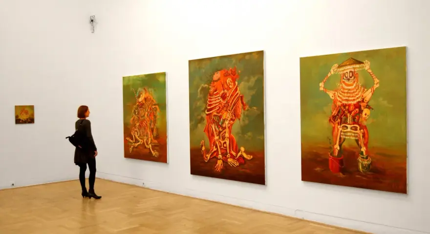 Kobieta podziwia surrealistyczne obrazy Jakuba Juliana Ziółkowskiego w galerii.