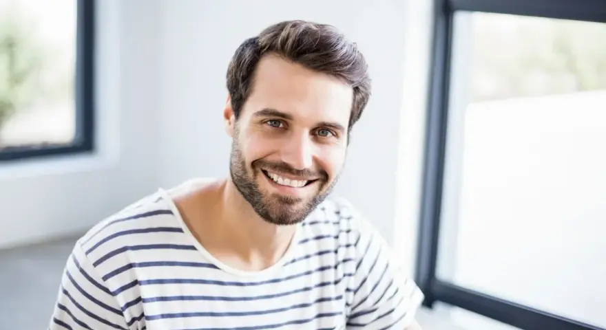 Uśmiechnięty mężczyzna o imieniu Marcin, z brodą i w pasiastym t-shircie, emanuje pozytywną energią. Znaczenie imienia Marcin to wojownik.