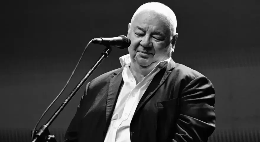 Czarno-białe zdjęcie Stanisława Sojki przy mikrofonie. Artysta z zamkniętymi oczami, w białej koszuli i marynarce, śpiewa. Stanisław Sojka nie żyje.