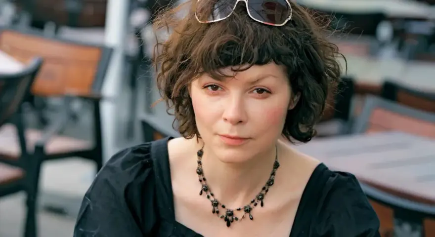 Agnieszka Glińska w czarnej sukience i naszyjniku, z okularami na głowie. Może wspominać swoich rodziców.
