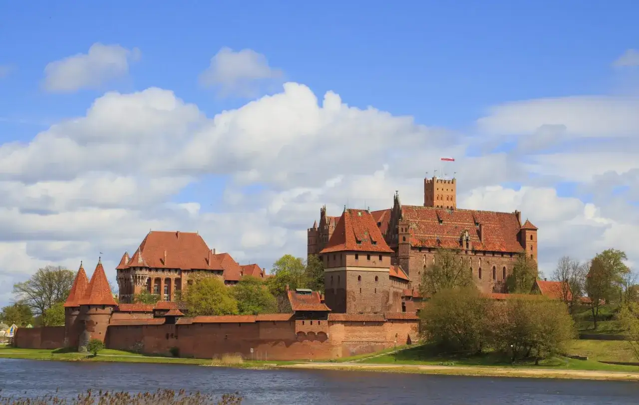 Potężny zamek w Malborku, kt&oacute;rego budowa rozpoczęła się w XIII wieku, g&oacute;ruje nad rzeką.