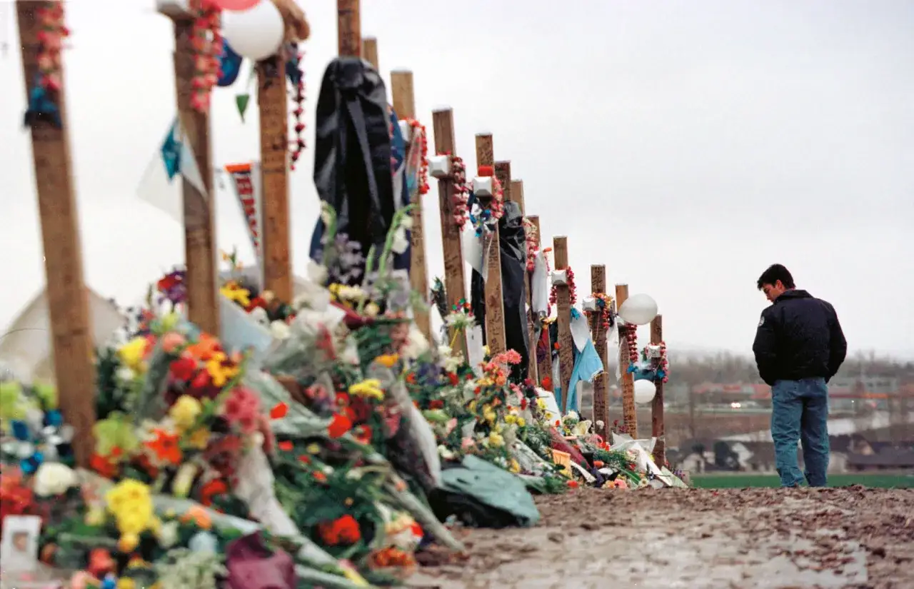 Pamięć o ofiarach masakry w Columbine High School. Krzyże ozdobione kwiatami i pamiątkami, mężczyzna pochylony w zadumie.