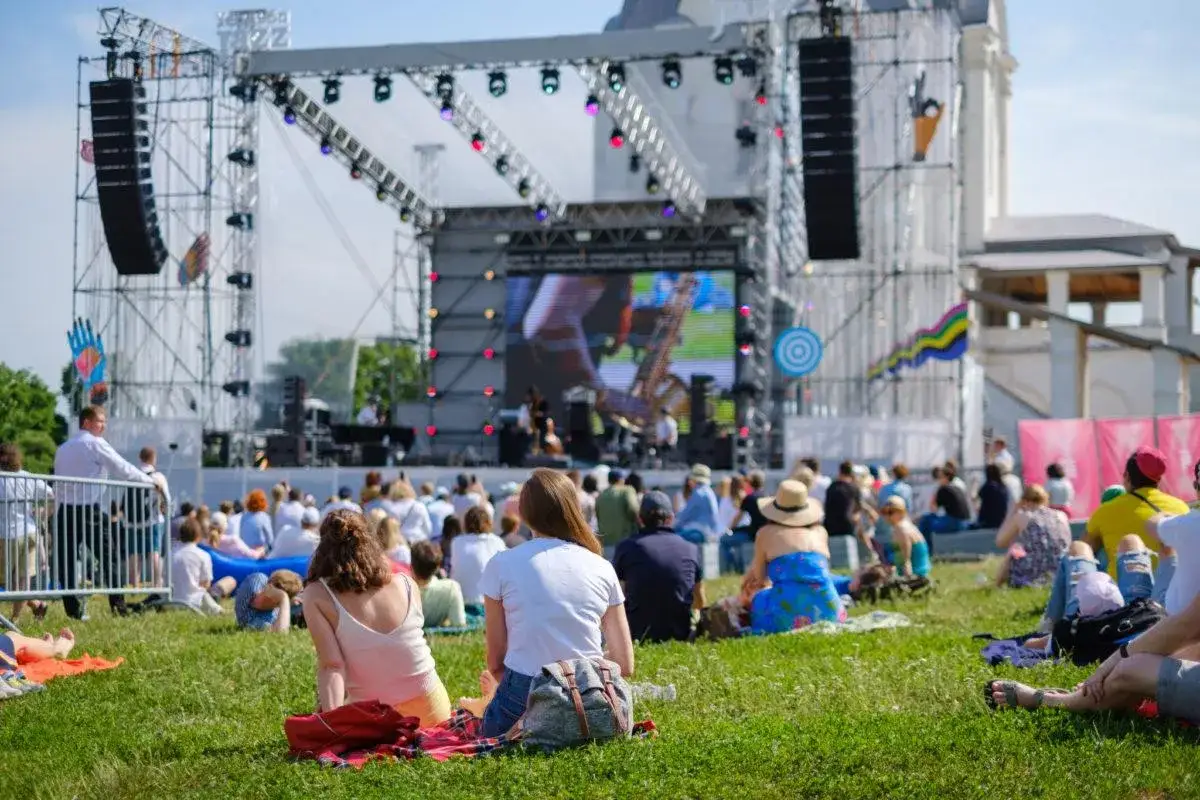 Tłum ludzi siedzi na trawie, oglądając koncert na dużej scenie. To jeden z wielu letnich festiwali w Polsce.