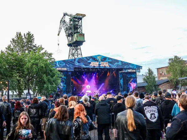 Tłum ludzi na koncercie pod wielkim dźwigiem. To jeden z wielu festiwali w Polsce, gdzie muzyka rockowa i metalowa przyciąga fanów.